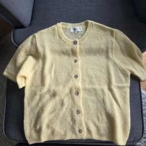 Gul stickad kofta från Monki - Söt ljusgul stickad kofta med korta ärmar och rund hals. Koftan har knappar framtill och är gjord i ett mjukt, fluffigt material som känns riktigt cozy. Perfekt att slänga över en topp för en chill look. Innehåller både ull och alpackaull. Mjuk och skön. Nypris: 400:- på Gina Tricot