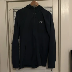 Svart vindjacka från Under Armour - Ljus blå/ mörk blå  vindjacka från Under Armour med luva och dragkedja framtill. Jackan har logga på bröstet och stort Under Armour-tryck på ryggen. Justerbar snörning vid luvan och två sidofickor. Perfekt för dig som gillar sportiga kläder och föredrar en clean loock. Har använt den två gånger och ser helt ny ut, vilket är anledningen till att den ligger på 600