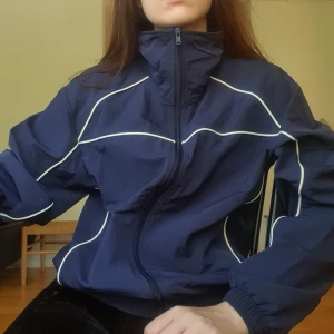 Mörkblå vindjacka med vita detaljer - Mörkblå vind-/sportjacka med vita kontrastlinjer och dragkedja. Oversized modell. Är storlek XXS men passar som en M eller 38.