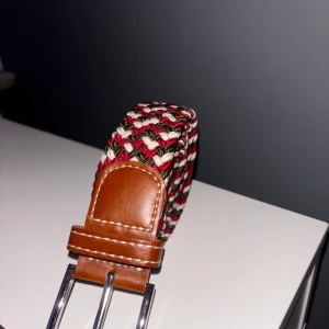  flätat bälte  - Snyggt flätat bälte i rött, vitt och grönt med bruna skinn-detaljer vid spännet.