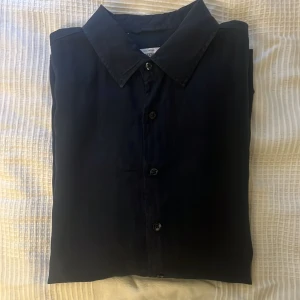 Mörkblå linneskjorta från Dressmann - Snygg marinblå skjorta från Dressmann i premium linne. Klassisk krage, långärmad och med knappar framtill i storleken Large. Perfekt för dig som gillar stilrena och enkla plagg med en avslappnad vibe.