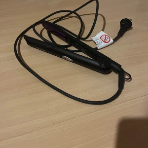 Svart plattång från Severin - En svart plattång från Severin med lila keramiska plattor och lång sladd. Plattången har en smal design med ett rött på/av-knapp.