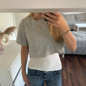 Grå croppad topp från New Yorker - Säljer en enkel och stilren grå croppad topp från new yorker. T-shirten har korta ärmar, rund halsringning och är tillverkad i mjuk bomull. Perfekt att matcha med jeans eller kjol för en avslappnad look. Pris kan diskuteras! OBS säljer endast t-shirten