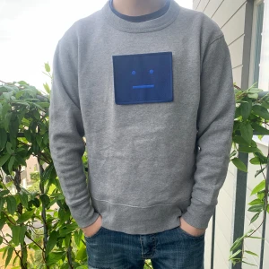 Grå sweatshirt från Acne Studios - Säljer en grå sweatshirt från Acne Studios med det ikoniska blå face-patch. Tröjan har rund hals, långa ärmar och är gjord i mjuk bomull. Perfekt för dig som gillar stilren design med en twist. Den släpptes år 2018 som en limiterad utgåva. Storleken är xxs, men passar dig som är mellan 165-172.