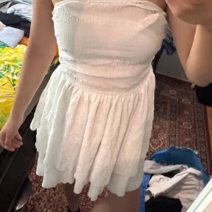 Vit axelbandslös volangkläning - Supersöt vit axelbandslös klänning med smockad överdel och volangig kjol. Storlek S, aldrig använd