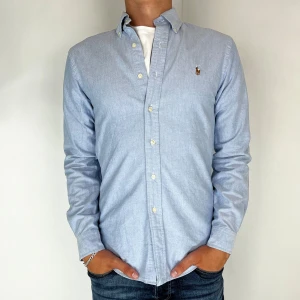 Ralph Lauren Skjorta  - Nu har vi nöjet att erbjuda en klassisk  skjorta från det välkända varumärket Ralph Lauren. Plagget är i storlek Small och är i mycket gott skick, utan några synliga defekter. Modellen på bilden är 182 cm lång och väger 75 kg, vilket kan ge en god indikation på tröjans passform.