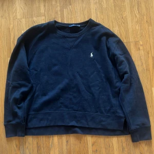Polo Ralph Lauren sweatshirt - Säljer en klassisk mörkare marinblå tröja från Polo Ralph Lauren med det ikoniska logotypbroderiet på bröstet. Tröjan har en rund halsringning och långa ärmar, perfekt för en stilren look.
