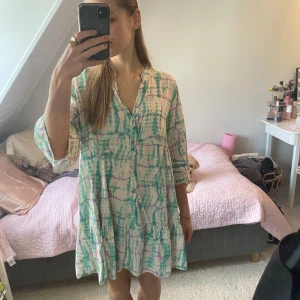 Mönstrad klänning med knappar - Säljer en färgglad klänning med ett unikt mönster i grönt och lila. Köpt på en marknad i Italien!🥰Klänningen har trekvartsärmar och knappar framtill. Luftig och härlig klänning. Står ingen storlek men skulle uppskatta den som M, själv brukar jag ha S förhållandevis😊
