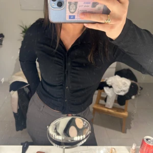 Svart ribbad topp - Säljer en stilren svart ribbad topp med knappar framtill. Koftan har en v-ringad design och långa ärmar. Smutsig spegel, ber om ursäkt för de😢