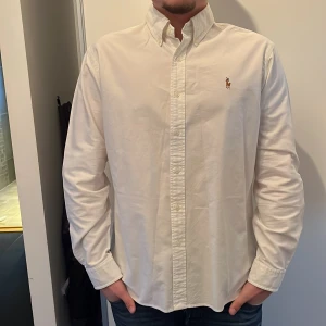 Vit skjorta från Ralph Lauren - Säljer en klassisk vit skjorta från Ralph Lauren i slim fit. Skjortan har långa ärmar och en broderad logotyp på bröstet. Perfekt för en stilren look.