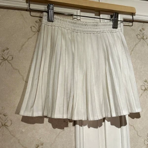 Vit plisserad kjol från Y.F.K. - Säljer en söt vit plisserad kjol från Y.F.K. med elastisk midja. Perfekt för en stilren och klassisk look. Passar bra till både vardag och speciella tillfällen.