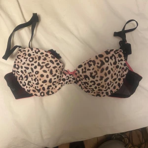 Leopardmönstrad bh  - Säljer en snygg bh med leopardmönster och rosa insida. Den har justerbara svarta axelband och en liten rosett framtill. Perfekt för att ge en färgklick till din garderob!