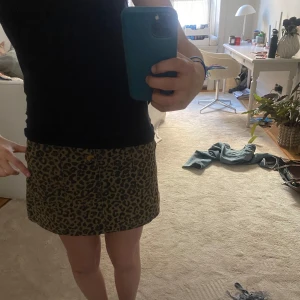 Leopardmönstrad kortkjol med knappar - Snygg leopardmönstrad kortkjol med knappar framtill. Perfekt för att ge din outfit en trendig touch. Kjolen har praktiska fickor och bälteshällor för extra stil.