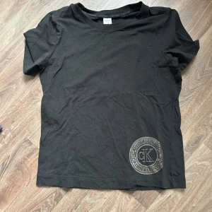 Svart t-shirt från Calvin Klein - Snygg svart t-shirt från Calvin Klein med deras ikoniska logga tryckt i nedre hörnet. Perfekt för en stilren look. T-shirten har en klassisk passform och korta ärmar.