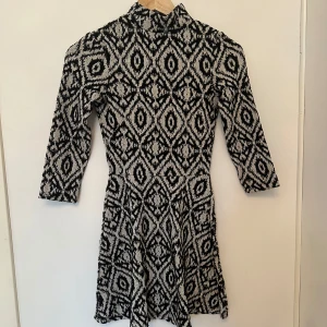 Svartvit mönstrad klänning - Snygg svartvit klänning med geometriskt mönster. Den har trekvartsärmar och en hög krage, vilket ger en stilren look. 