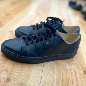 Mörkblåa sneakers från Axel Arigato - Snygga mörkblåa sneakers från Axel Arigato med diskret guldfärgad logga på sidan. Skorna har en stilren design med snörning och är tillverkade i skinn. Perfekta för en minimalistisk look. Är använd ett fåtal gånger och är som nya. Ny pris på skorna är ca 2400kr