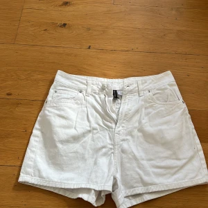 Vita shorts från H&M Divided - Säljer ett par vita shorts från H&M Divided i storlek 36. De är tillverkade i 100% bomull och har en klassisk femficksdesign med knapp och dragkedja framtill. Perfekta för en avslappnad sommarlook! Ej stretch!