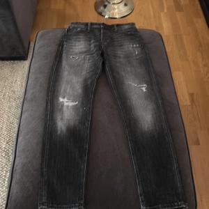 Mörkgråa jeans från Jack & Jones - Snygga mörkgråa jeans från Jack & Jones med en cool slitningseffekt. De har en tapered passform och är perfekta för en avslappnad stil. Jeansen har en klassisk femficksdesign och är tillverkade i ett slitstarkt denimtyg.
