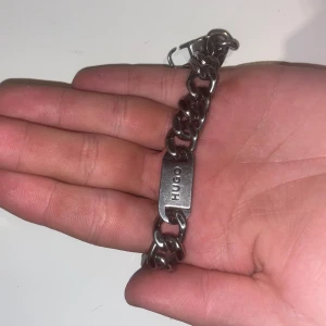 Silverfärgat armband från Hugo - Snyggt och robust silverfärgat armband från Hugo med breda länkar och en platta med logotyp. Perfekt för att ge en stilren touch till din outfit.