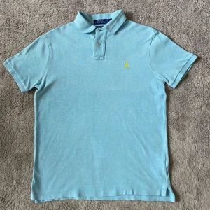 Ralph Lauren piké - Säljer en snygg ljusblå pikétröja från Ralph Lauren i storlek M. Tröjan har en klassisk krage med två knappar och det ikoniska broderade logotypen i gult på bröstet. Perfekt för både vardag och fest! 💙Nypriset är cirka 1100 kr i mycket bra skick! 