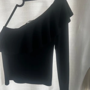 Svart oneshoulder topp - Snygg svart oneshoulder topp med volangdetalj från Gina. Tajt fit❤️