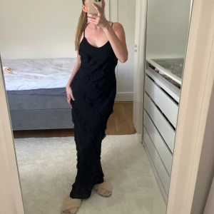 Svart långklänning med volangdetaljer - Elegant svart långklänning med smala axelband och volangdetaljer. Perfekt för en stilren look. Fungerar både för xs och s 