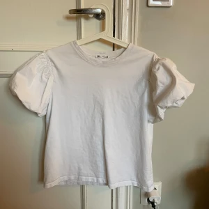 Vit t-shirt från Zara - Säljer en vit t-shirt från Zara med puffiga korta ärmar. Perfekt för en stilren och enkel look. Tillverkad i mjukt bomullsmaterial för extra komfort. I storlek L