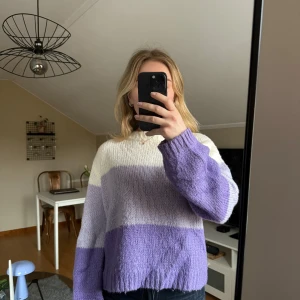 Randig stickad tröja NA-KD - Säljer en mysig stickad tröja från NA-KD x Emilie Malou i randigt mönster med färgerna lila, vit och beige/vit. Tröjan har en avslappnad passform med långa ärmar och en rund halsringning. Perfekt för kyliga dagar!