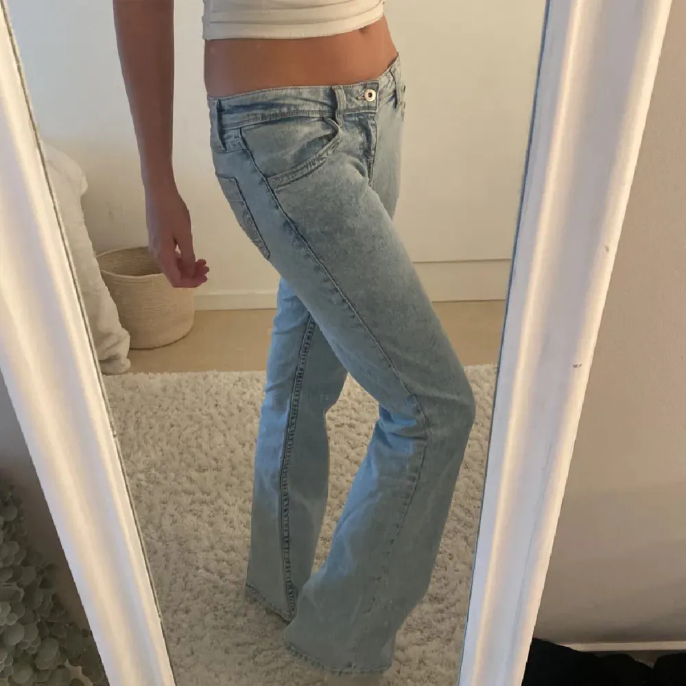 Säljer ett par ljusblå bootcut jeans med klassisk femficksdesign och knappgylf. Jeansen har en snygg tvättad look och är perfekta för en avslappnad stil. De är lågmidjade och har en bekväm passform.. Farkut & Housut.
