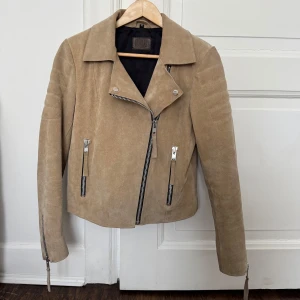 Beige mockajacka  - Snygg beige mockajacka med dragkedja och flera dragkedjedetaljer. Jackan har en klassisk krage och långa ärmar med dragkedjor vid ärmsluten. 