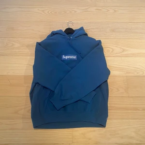 Blå hoodie från Supreme - Säljer en snygg blå hoodie från Supreme med klassisk logga på bröstet. Hoodien har en känguruficka och en justerbar huva. Perfekt för en casual look eller streetwear-stil. Nypris är cirka 2000 kr. Skriv om ni har några funderingar. *VARAN ÄR ÄKTA*