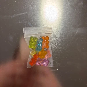 Färgglada björnformade pärlor - Säljer ett set med små björnformade pärlor i olika färger som grön, blå, orange, röd och rosa. Perfekta för att skapa egna smycken eller accessoarer. Pärlorna är förpackade i en liten plastpåse.