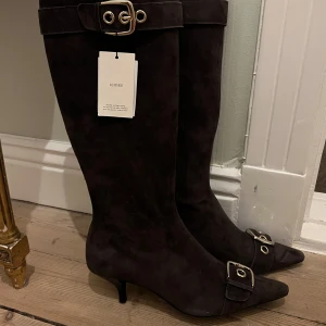 Bruna mockastövlar med spänne - Eleganta bruna  stövlar i mocka med spetsig tå och dekorativa spännen. Perfekta för en stilren look.