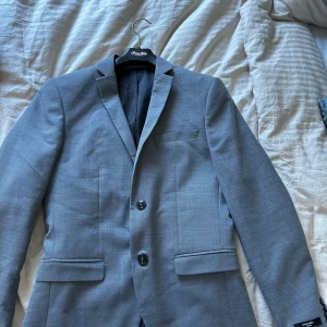 Grå kostym från Cavaliere - Snygg grå kostym från Cavaliere med kavaj och matchande byxor. Kavajen har två knappar och klassiska fickor. Perfekt för formella tillfällen. Kavaj storlek är 44 byxorna är 48