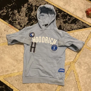 Ljusblå hoodie från Hoodrich - Säljer en ljusblå hoodie från Hoodrich med tryck och patchar på framsidan. Tröjan har en stor huva och en praktisk magficka. Perfekt för en avslappnad stil.