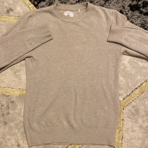 Beige stickad tröja från Uniqlo - Säljer en stilren beige stickad tröja från Uniqlo. Tröjan har en rund halsringning och långa ärmar med ribbade muddar. Perfekt för en avslappnad och bekväm stil.