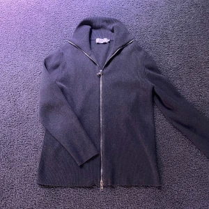 Grå zip  - Säljer en stilren grå ribbad tröja från Ljung med dragkedja framtill. Tröjan har en hög krage och långa ärmar, perfekt för kyligare dagar. Passar bra till både jeans och chinos. 