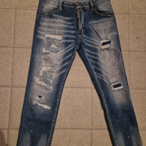 Blå slitna skinny jeans med hål - Säljer ett par blå skinny jeans med slitningar och hål på både fram- och baksida. Jeansen har en tvättad look med ljusa partier och små färgstänk. Klassisk femficksmodell och dragkedja i gylfen. Perfekta för en avslappnad streetstil. Pris kan diskuteras via dm