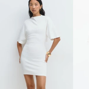 Vit kort tie back dress från Gina Tricot  - Helt ny, med lapp kvar. Superfin vit kort klänning med breda ärmar och snygg knytning i ryggen (som man kan justera/knyta själv). Klänningen har en figurnära passform och hög hals. Materialet är mjukt och stretchigt. Den är i storlek XS men funkar också som S då den är stretchig. 