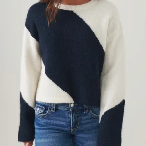 Svartvit stickad tröja från Gina  - Säljer en stickad tröja i svart och vitt med coolt blockmönster i diagonal design. Tröjan har rund halsringning och långa ärmar. Den är mjuk och lite fluffig, perfekt för att ge din outfit en trendig touch.