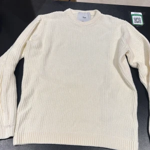 Krämvit stickad tröja från Use - Säljer en krämvit stickad tröja från Use i storlek L. Tröjan har rund halsringning, ribbade muddar och är tillverkad i 100% bomull. Perfekt för lager-på-lager och enkel att matcha med jeans eller kjol.