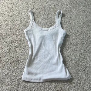 Vit ribbad linnetopp Gina Tricot XS - Säljer en vit ribbad linnetopp från Gina Tricot, Basically Basics-kollektionen. Toppen har smala axelband och är figurnära med stretchigt material. Perfekt att styla med jeans eller kjol för en clean look.