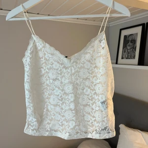 Vit spetslinne med blommönster H&M - Superfint vitt linne från H&M i storlek S, med tunna axelband och v-ringad spetskant. Hela toppen är täckt av ett blommigt spetsmönster som ger en romantisk vibe. Perfekt att styla med jeans eller kjol för en fräsch look. PRISLAPP ALDRIG ANVÄND! 