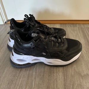 Buffalo chunky svarta sneakers strl 39 - Buffalo sneakers i svart med chunky vit sula och coola detaljer. Ovandel i mesh och syntet med snörning och logga på plösen. Riktigt trendig och sportig look som sticker ut. Perfekta för dig som gillar streetstyle och vill ha bekväma skor med attityd.