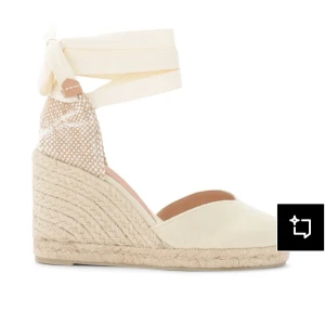 Beige espadrille wedges med knytband - Snygga espadrille wedges i beige med flätad platå och höga klackar. Skorna har rund tå, canvasmaterial och breda knytband runt ankeln. Baksidan är mönstrad i naturtoner och sulan är i repimitation för en somrig vibe. Använda bara en gång och i väldigt bra skick!!