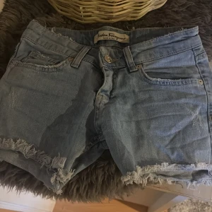 Jeansshorts Ferragamo med paljettficka - Snygga ljusblå jeansshorts från Salvatore Ferragamo med råa, fransiga kanter och en unik bakficka dekorerad med paljetter och broderade detaljer. Klassisk femficksmodell och knappgylf. Perfekta för sommaren och ger en cool, avslappnad vibe. Pris kan diskuteras💕