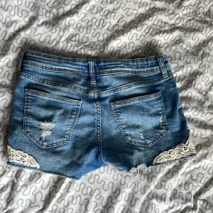 Blå jeansshorts med spets från H&M - Snygga blå low waist jeansshorts från H&M med slitna detaljervibe.
