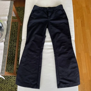 Lågmidjade kostymbyxor - Svarta bootcut byxor från Gina Tricot i storlek 36. Klassisk modell med hällor för bälte, dragkedja och knapp framtill. Snyggt utsvängda ben och stilren look, perfekta till sneakers eller boots.