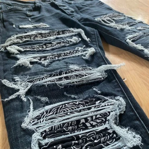 Amiri Jeans - Riktigt snygga svarta skinny jeans från Amiri med stora slitningar och patchade detaljer i svartvitt mönster under trasorna. Jeansen har klassisk femficksdesign och cool streetkänsla. Perfekta för dig som vill sticka ut med en edgy stil. OBS metall tag på backre sida har tagits bort.