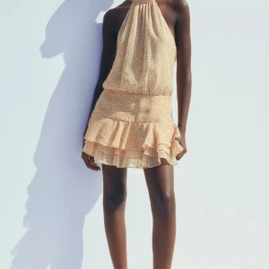 Ljusblommig kort halterneckklänning - Superfin kort klänning från Zarai ljusgul med små blommor i oranget. Halterneck med öppen rygg och volangkantad kjol. Luftigt material, perfekt för varma dagar. Sitter så fint  och har en flowy känsla. Den är slutsåld på hemsidan. Storlek m, helt ny med lapp kvar🌸💞